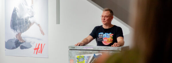 Tamminen puhuu sähköboksista tehdyn puhujapöntön takana. Taustalla H&V-vastamainos.