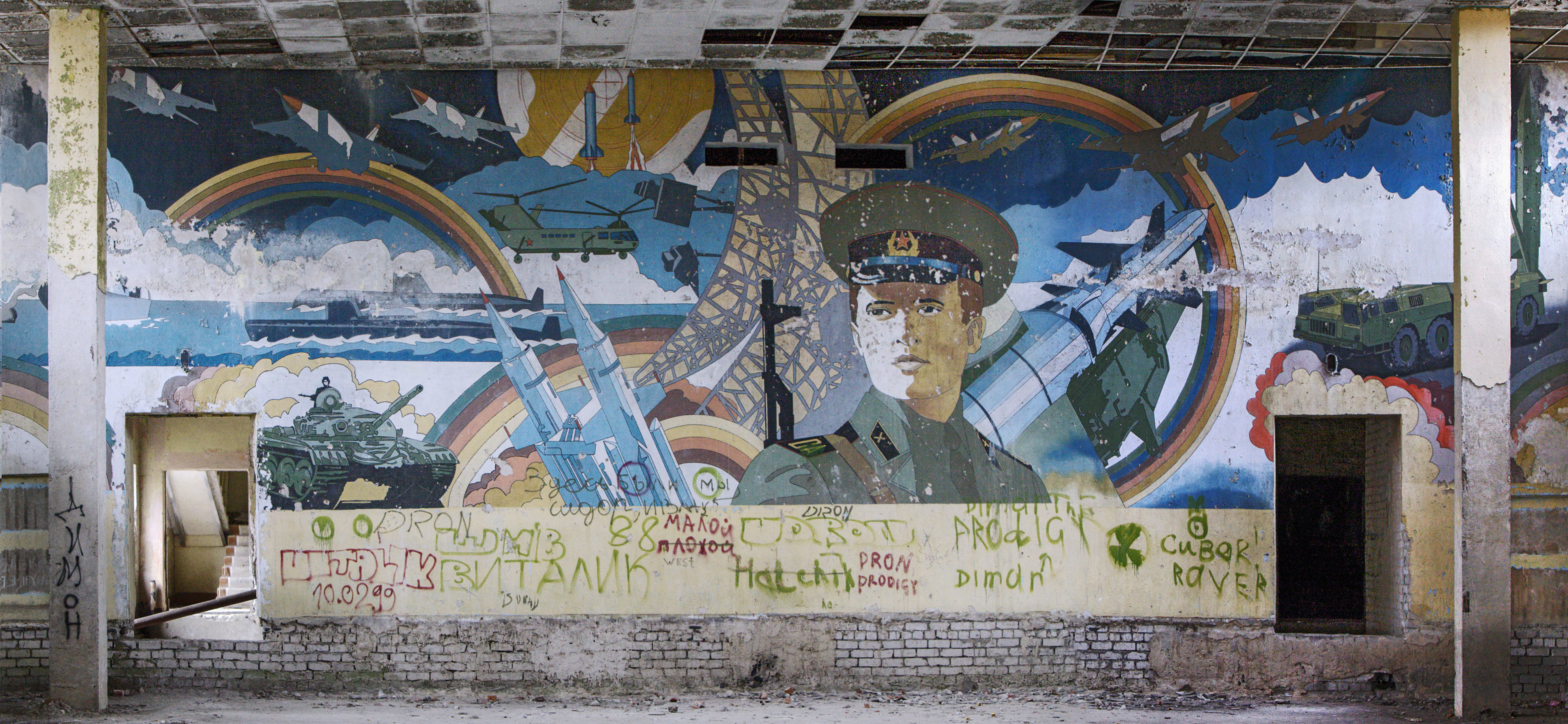 Neuvostoliittolainen muraali joka kuvaa maan sotilasmahtia. Muraalin alla graffiteja ja tägejä.