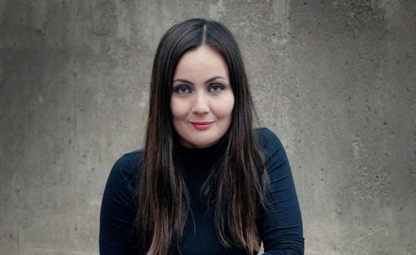 Emilia Kukkala katsoo kameraan hymyillen, taustalla harmaa seinä.