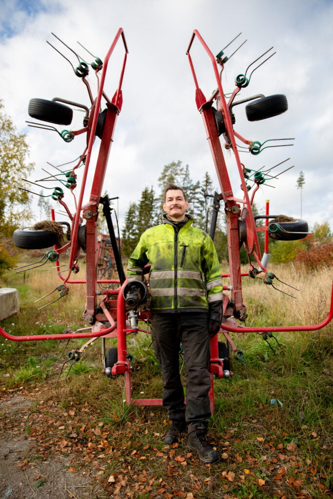 Kyrö seisoo, katsoo kameraan, nojaa työkoneeseen.