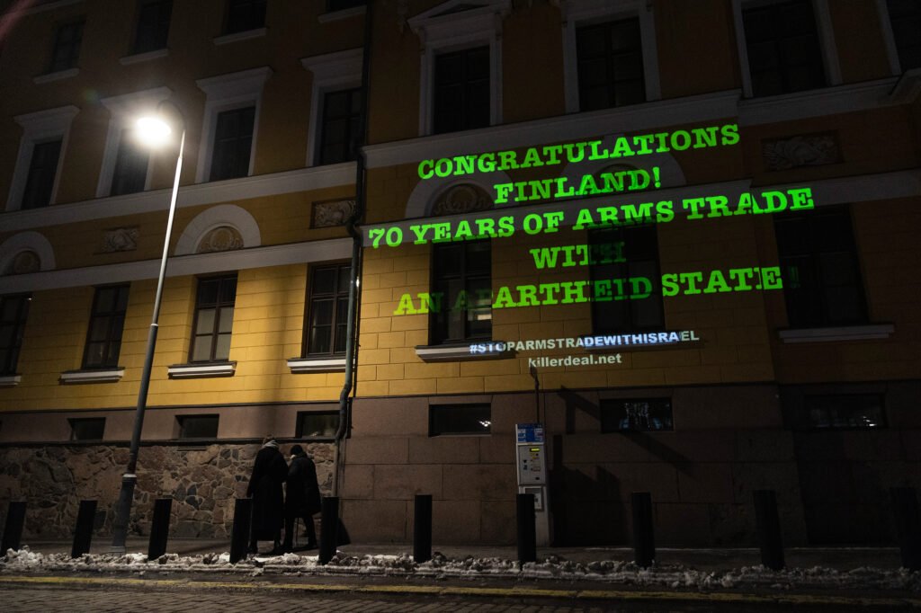 Teksti "Congratulations Finland! 70 Years of Arms Trade with an Apartheid State" heijastettuna puolustusministeriön seinään.