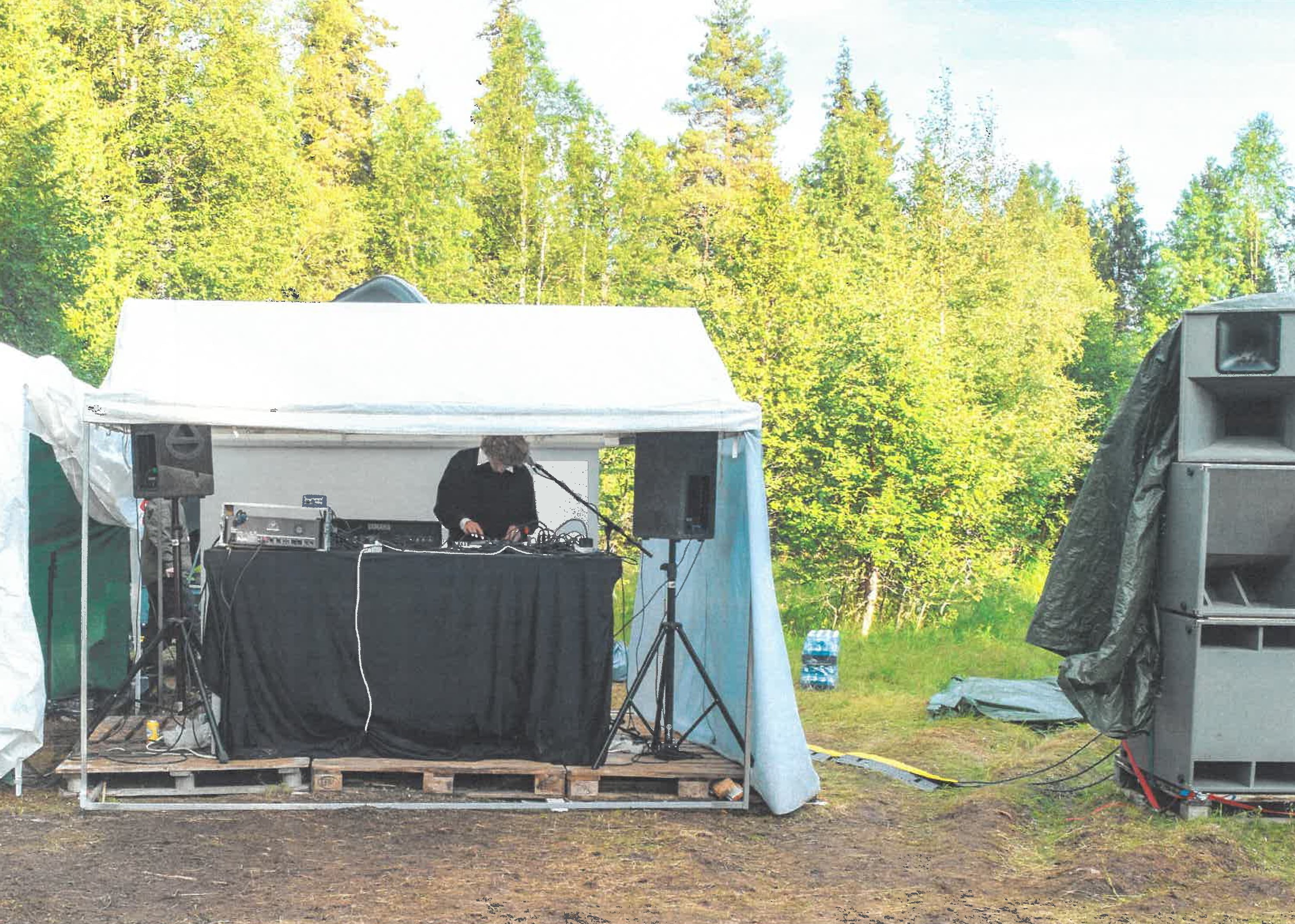 Pieni kuormalavoista rakennettu lava ja teltta. Henkilö soittaa musiikkia.